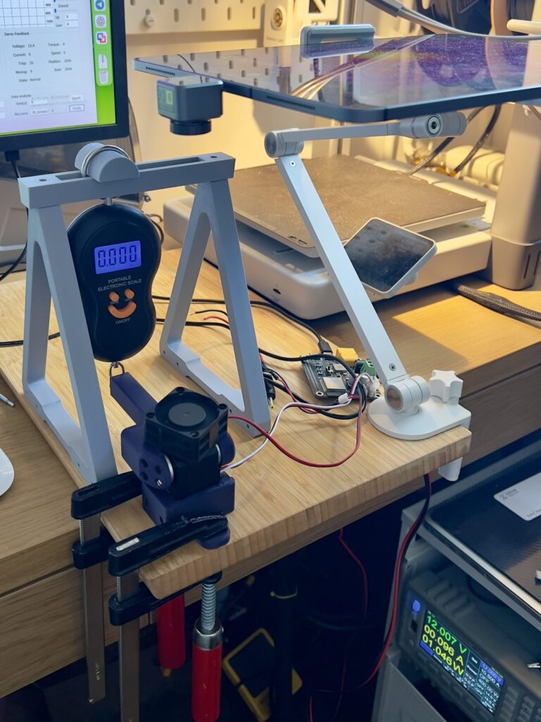 Maximum torque test stand: a 3D-printed frame holds a digital hanging scale against a 10 cm lever on the servo horn with a 12 V bench supply
